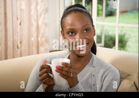 Young African woman sitting on a couch, enjoying a hot beverage Stock Photo