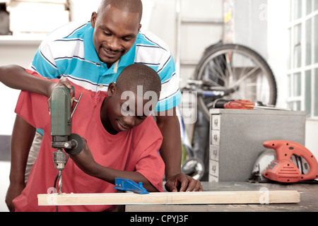 African Father and son using a drill in a workshop Stock Photo