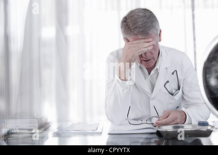 Doctor rubbing his forehead in office Stock Photo