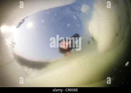 Diver looking into an ice hole, subglacial diving, ice diving, in the frozen Black Sea, a rare phenomenon Stock Photo