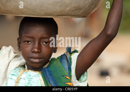 A girl who doesn't go to school carries a metal bin on her head in the village of Djorbana, Zanzan region, Cote d'Ivoire Stock Photo