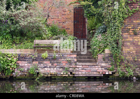 a wooden seat next to stairs leading down from a doorway to a river or canal Stock Photo