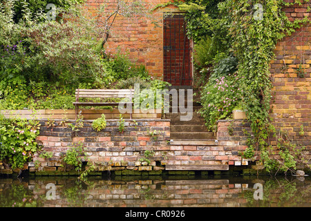 a wooden seat next to stairs leading down from a doorway to a river or canal Stock Photo
