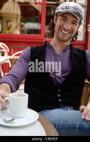 Man, early 30s, wearing casual clothes sitting in an outdoor café with a coffee cup, smiling Stock Photo