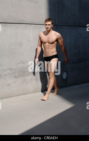 Young man wearing bathing trunks, walking in front of a concrete wall Stock Photo