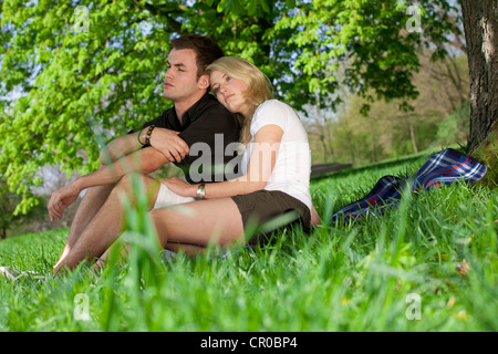 Young couple sitting on a picnic blanket under a tree in a park in spring Stock Photo