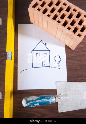 Trowel, spirit level and a brick on a drawing of a house Stock Photo