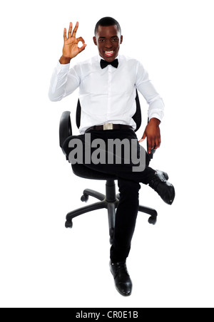 Successful african corporate man sitting on chair and showing okay gesture to camera Stock Photo