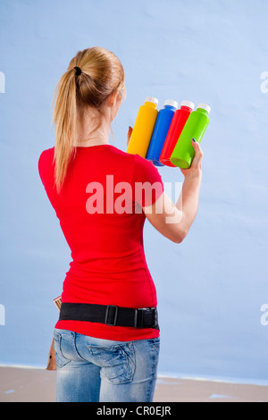 Young woman holding several tubes of paint in her hands in front of a wall Stock Photo