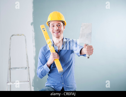 Young tradesman holding a spirit level and a trowel Stock Photo