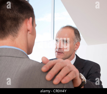 Senior colleague, serious, putting hand on younger colleague's shoulder Stock Photo