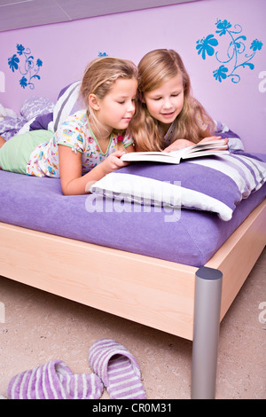 Two girls, sisters reading in bed Stock Photo
