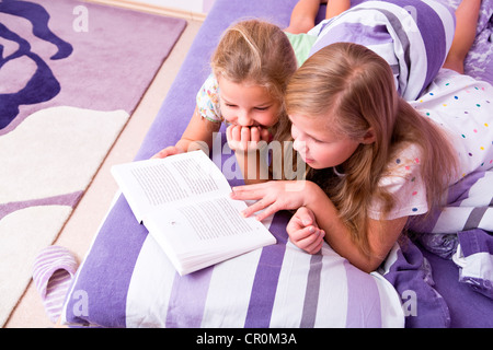 Two girls, sisters reading in bed Stock Photo
