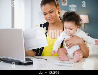 Mixed race mother holding baby and paying bills Stock Photo