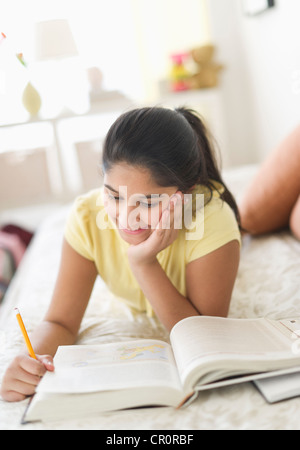 USA, New Jersey, Jersey City, Girl (12-13) lying on bed and studying Stock Photo