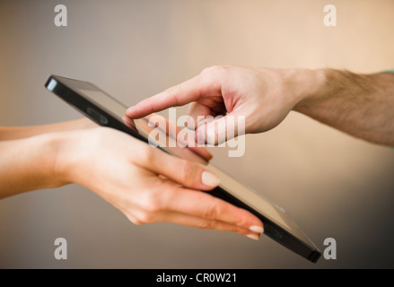 Close up of man's and woman's hands using digital tablet, studio shot Stock Photo