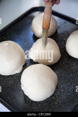 Man Coating Bread dough with milk glaze before baking Stock Photo
