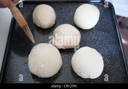 Man Coating Bread dough with milk glaze before baking Stock Photo