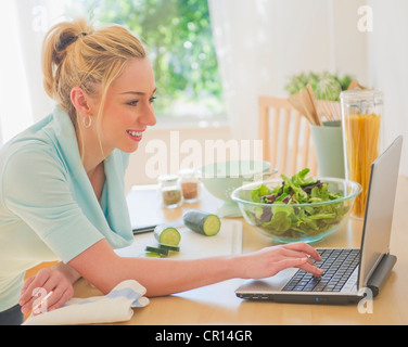 USA, New Jersey, Jersey City, Smiling young woman using laptop in kitchen Stock Photo
