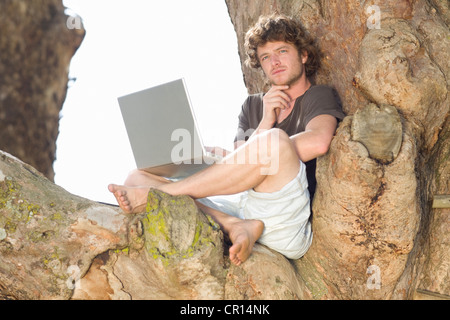 Pensive man using laptop in tree Stock Photo