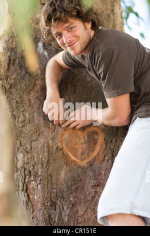 Smiling man carving heart in tree Stock Photo