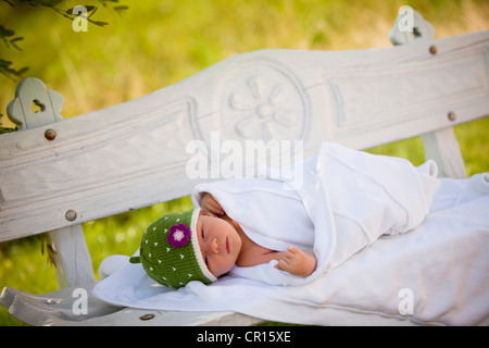 Newborn baby girl, two weeks old, lying on an outdoors bench Stock Photo