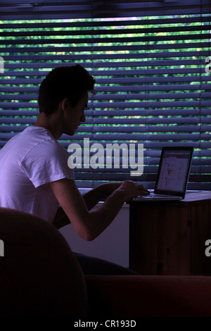 Young male sitting in a dark room using a laptop. Stock Photo