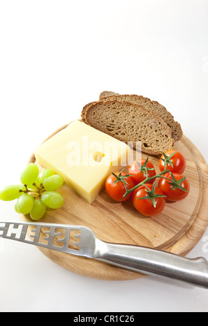 Emmental cheese on a board with grapes, bread and tomatoes Stock Photo