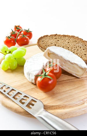 Camembert cheese on a board with grapes, bread and tomatoes Stock Photo