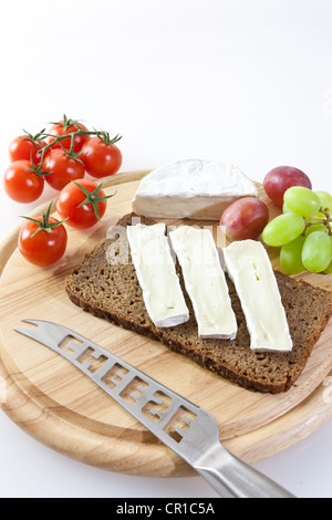 Camembert cheese on a board with grapes, bread and tomatoes Stock Photo