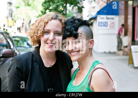 two smiling adult sisters, one with punk haircut, pose for portrait on side street in Hells Kitchen neighborhood New York City Stock Photo