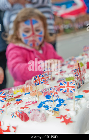 Cakes, bunting, face paint and champagne are enjoyed at a street party in South West London despite the odd burst of rain. Stock Photo