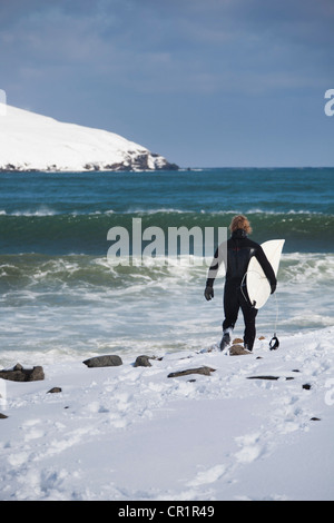 Surfer carrying surfboard on snowy beach Stock Photo