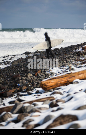 Surfer carrying surfboard on snowy beach Stock Photo