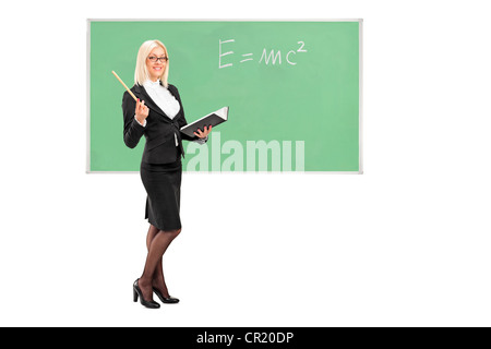 Full length portrait of a female teacher with a book in her hand and chalkboard in the background Stock Photo