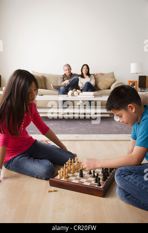 USA, California, Los Angeles, Siblings playing chess game while parents watching from sofa Stock Photo
