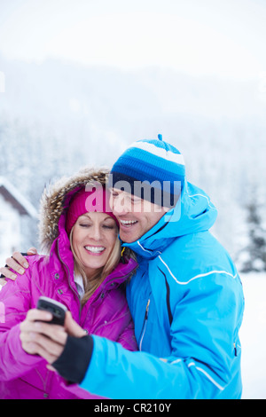 Couple using cell phone together in snow Stock Photo