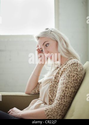 Thoughtful young woman sitting on sofa Stock Photo
