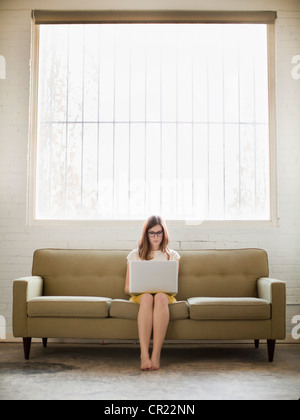 Young woman sitting on sofa with laptop Stock Photo