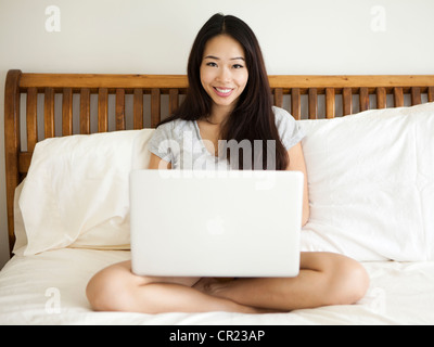 Young woman sitting on bed, using laptop Stock Photo