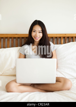 Young woman sitting on bed, using laptop Stock Photo