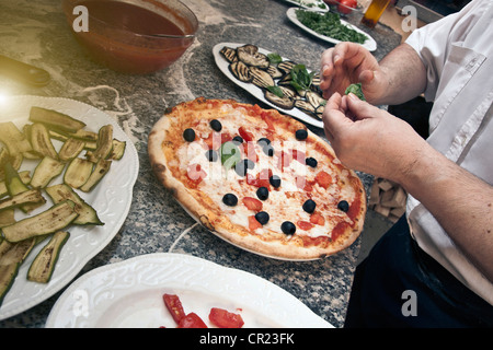 Chef garnishing pizza in kitchen Stock Photo