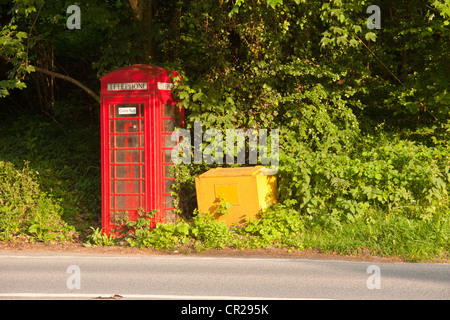 Old fashioned red telephone box with yellow grit container on Devon country road. Stock Photo