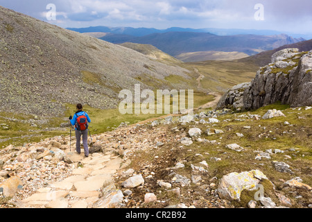 A hiker descends the steep path from the summits of Ill & Broad Crag in the Lake District. The Langdale Pikes can be seen in the