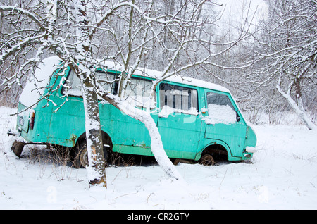 Old broken minibus covered with snow in winter garden near apple trees. Stock Photo