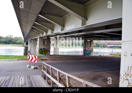 road sign indicating direction of movement under large metal bridge over river. Stock Photo