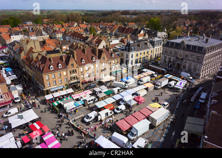 A weekly street market in Bergues, France, seen from a tower overlooking the main square. There are French market stalls and the Mairie or Town Hall. Stock Photo