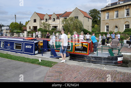 Two narrowboats negotiate Bradford on Avon lock on the Kennet and Avon Canal together, while a crowd of spectators look on. Stock Photo