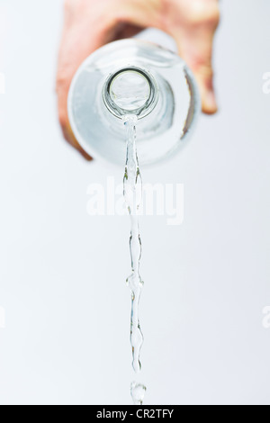 Hand pouring mineral water from a glass bottle against white background