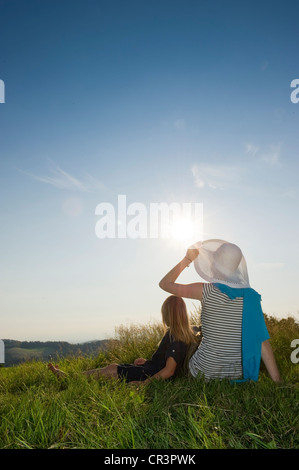 Woman and child sitting on a meadow with the sun shining, Black Forest, Baden-Wuerttemberg, Germany, Europe Stock Photo